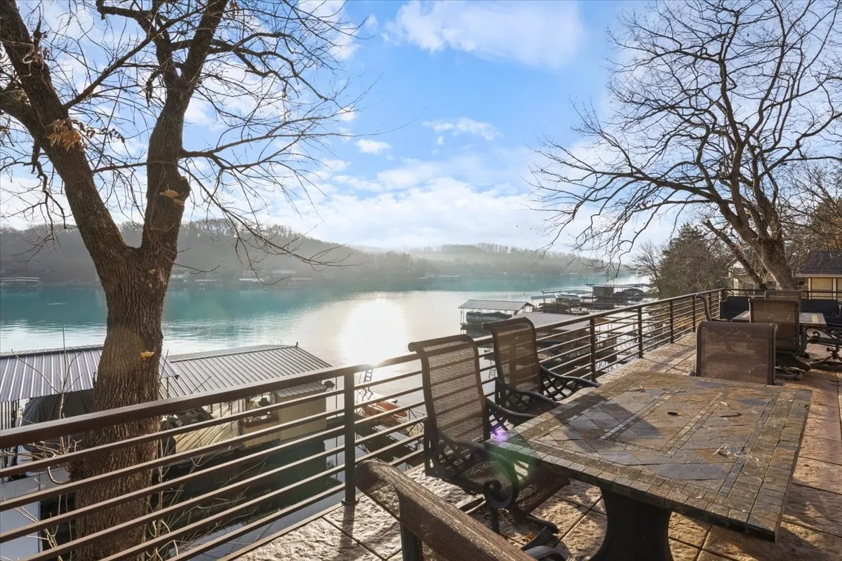 A peaceful outdoor patio area with comfortable seating and a table overlooking the lake, framed by bare trees. The setup invites guests to relax, dine outdoors, and enjoy sunset or sunrise views with loved ones, making it ideal for memorable social gatherings.