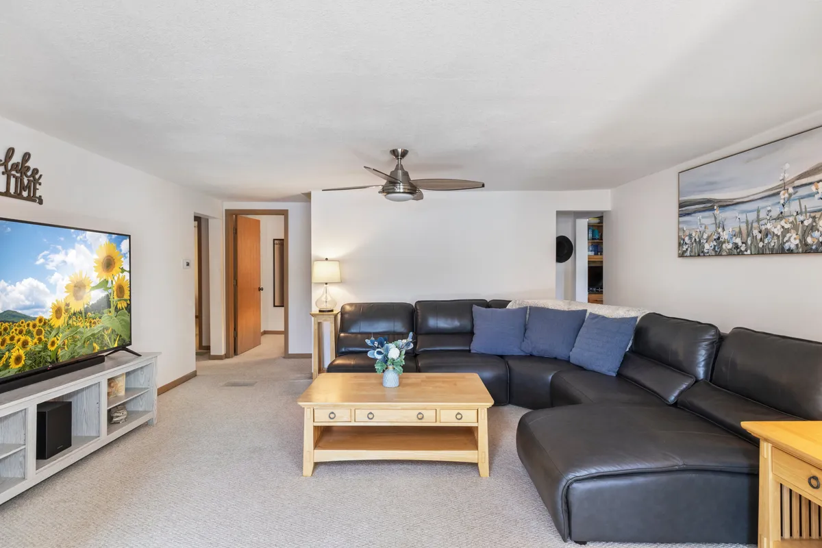 A modern, inviting living room with a large sectional sofa, flat-screen television, decorative artwork, and a wooden coffee table. The layout encourages family movie nights, socializing, and provides plenty of space for pets to stretch out.