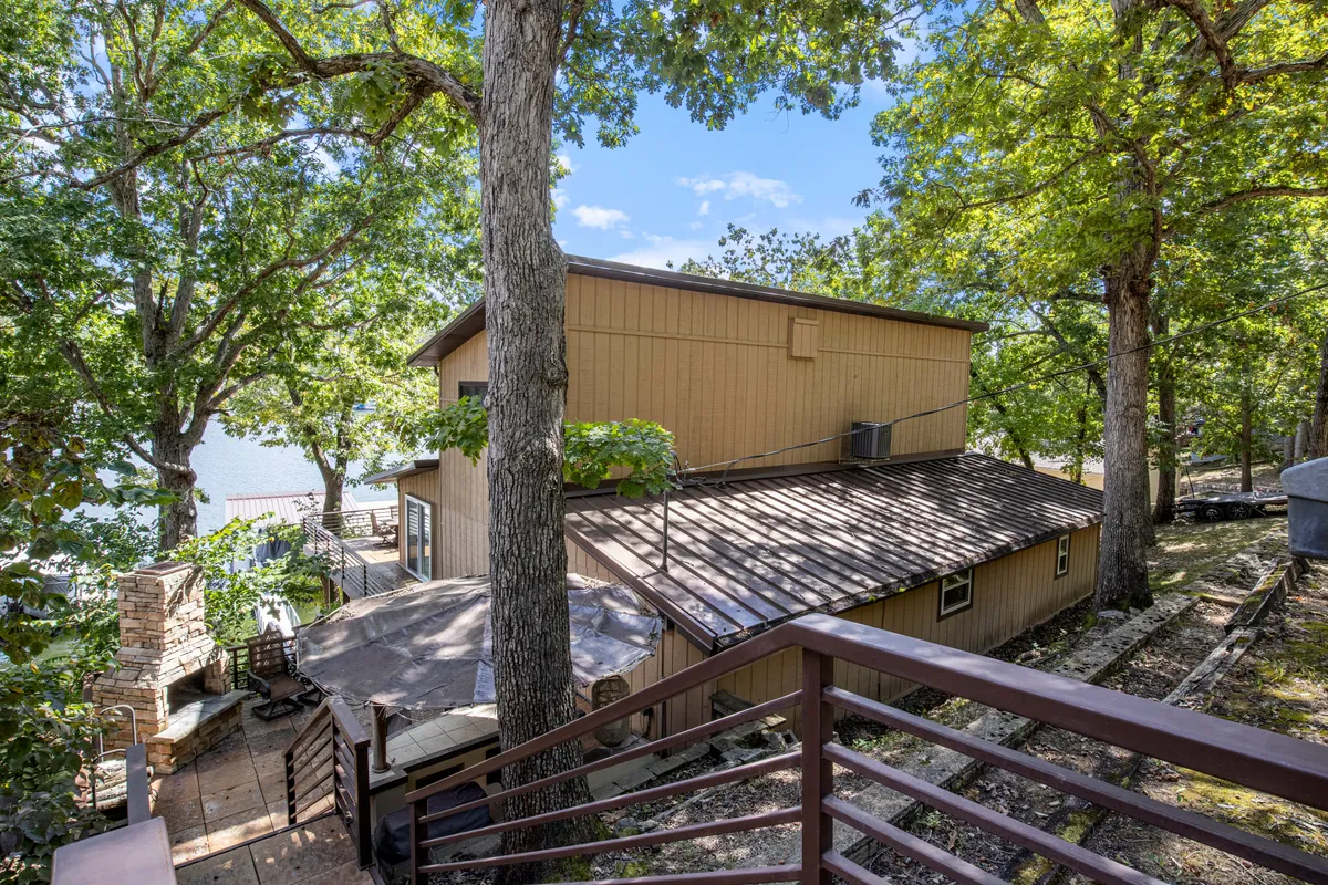 A peaceful exterior view of the house nestled among trees beside the lake. The image highlights the proximity of the home to nature and water, with inviting outdoor spaces. It conveys a sense of calm and the potential for lakeside relaxation, barbecues, or playtime with pets.