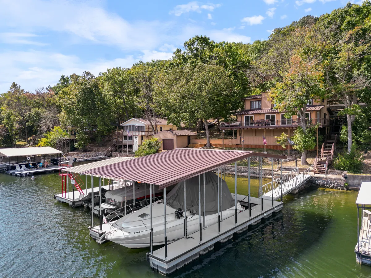 A scenic lakeside view showing a well-kept dock with a boat, adjacent to a waterfront house surrounded by mature trees. The inviting waterfront setting is ideal for boating, fishing, or relaxing, enhancing the sense of a personalized lake getaway.