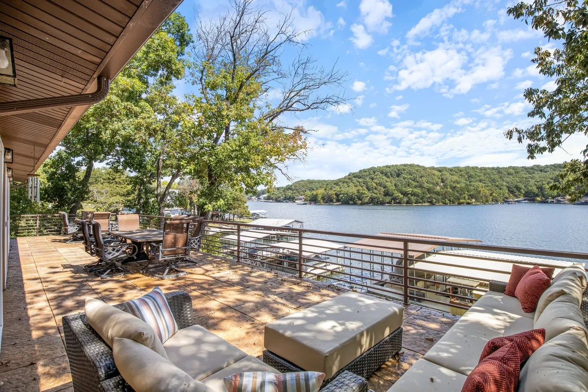 This image showcases a serene deck seating area overlooking the lake, framed by surrounding trees. The space appears inviting for both people and pets, offering a sense of openness and a direct connection to the outdoors. The deck is spacious and seems to be an ideal spot for relaxing, entertaining, or simply enjoying the tranquility of lakeside life with furry companions.