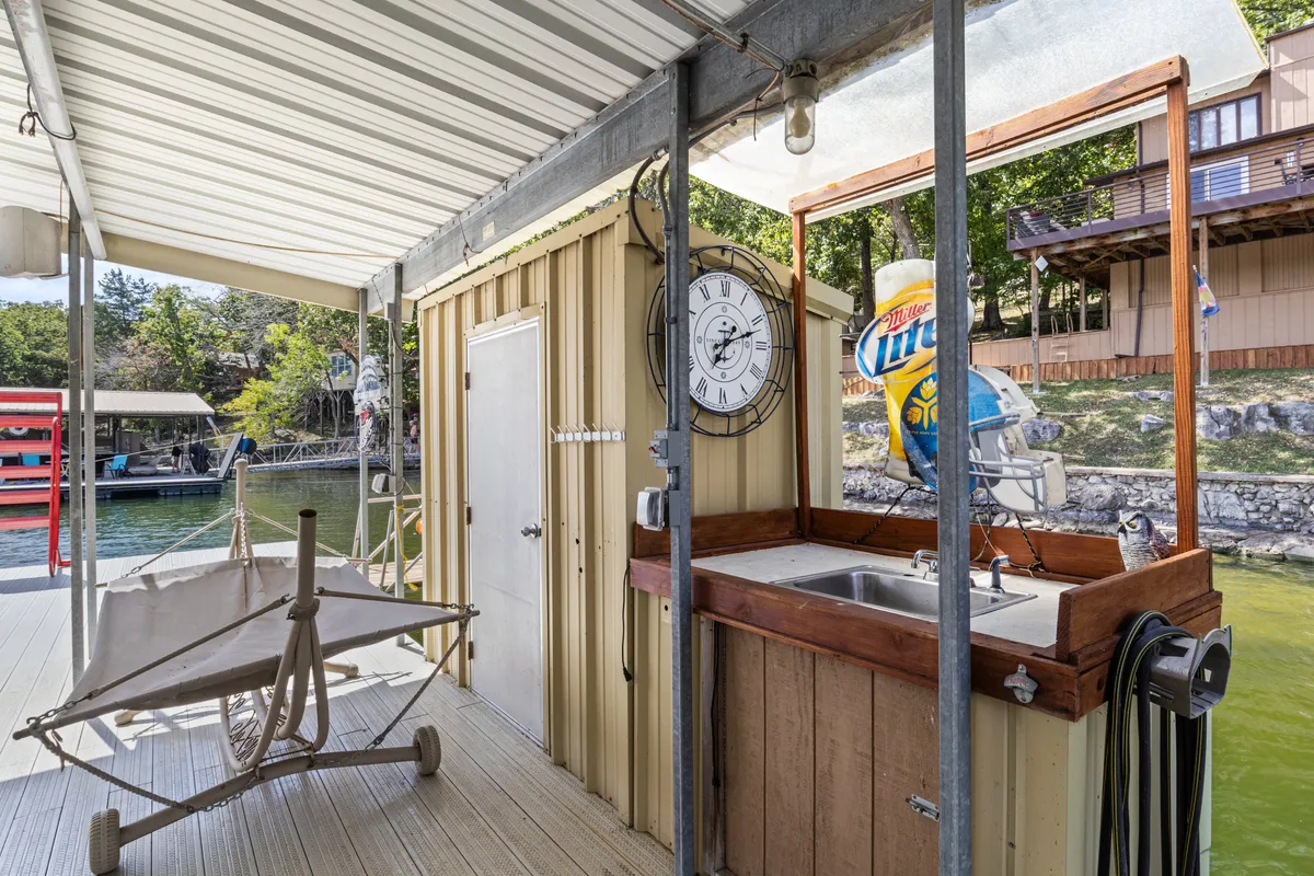 A casual bar area by the water featuring a hammock, a sink, and inviting seating with a view of the lake. The relaxed atmosphere suggests a perfect spot for après-water activities and socializing as the sun sets.
