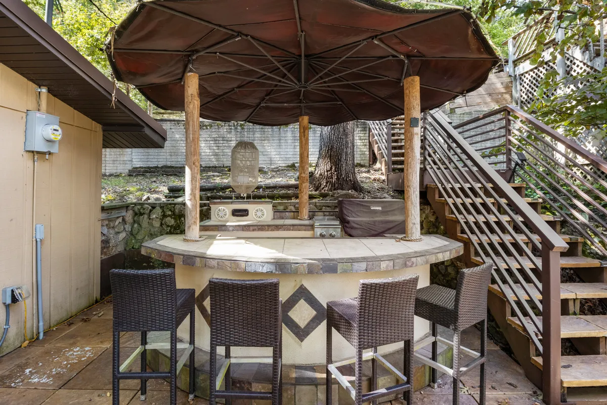 This image showcases a vibrant outdoor bar area complete with bar stools, a decorative stone wall, and lush surrounding greenery. The bar is clearly the gathering spot, ideal for socializing and enjoying drinks outdoors, and the setting is casual and welcoming.