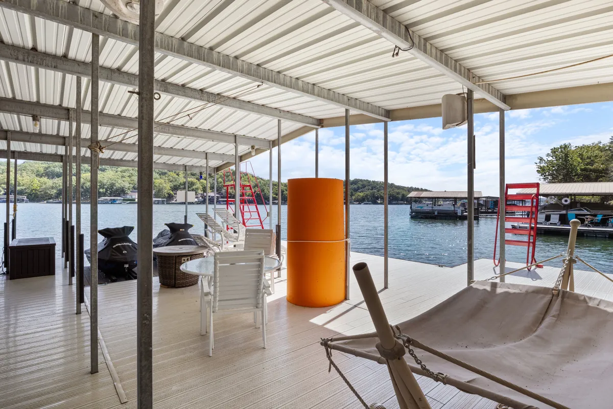 A relaxed lakeside scene featuring cozy chairs, a hammock, and a unique orange cylindrical structure, all positioned to take in expansive water views. The setting is casual and welcoming, ideal for unwinding or socializing by the lake.