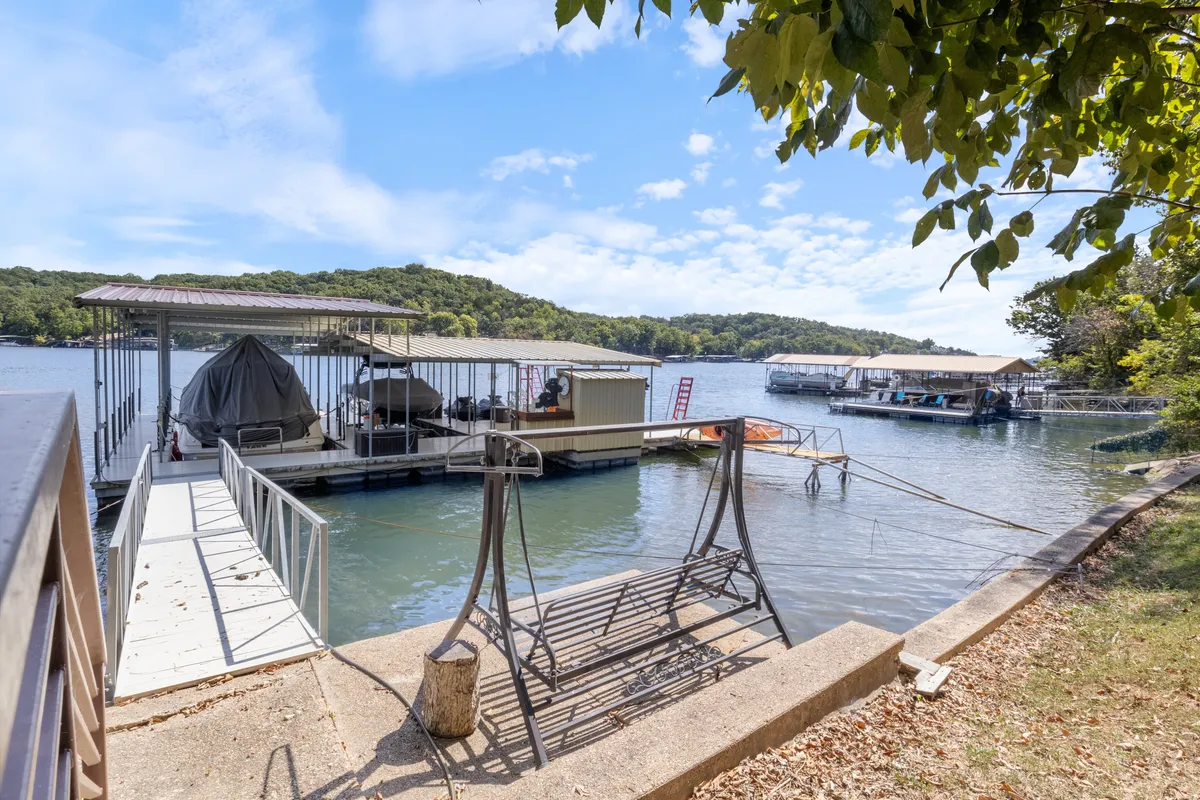 A serene dock stretches out over calm water, with boats moored and surrounded by lush trees. The dock is spacious enough for both relaxation and water sports, and the tranquil mood is enhanced by the promise of sunset views.
