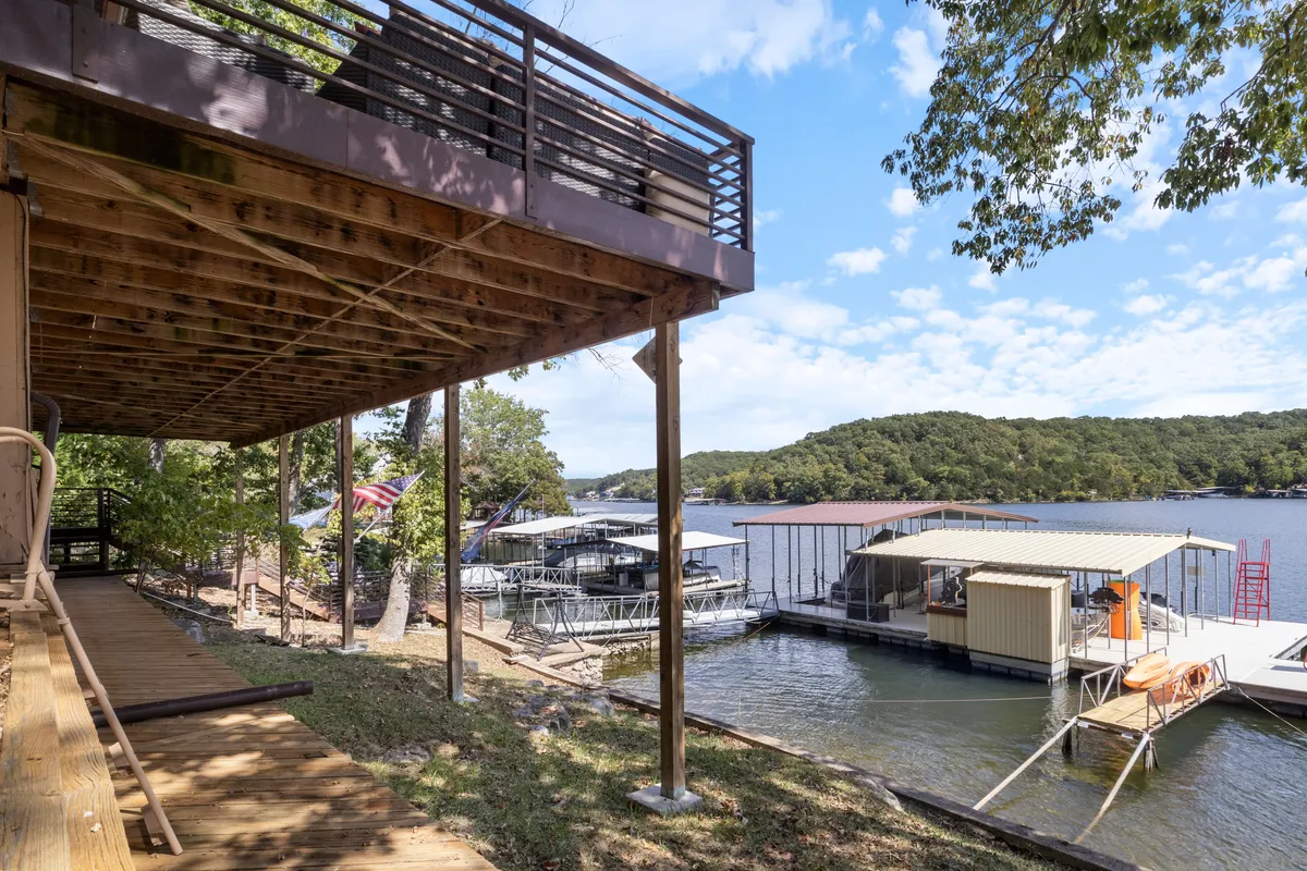 A peaceful lakeside scene with a deck overlooking the water, boathouses, and docks with boats moored. Surrounding greenery frames the tranquil setting, ideal for fishing, sunbathing, or simply unwinding by the water.