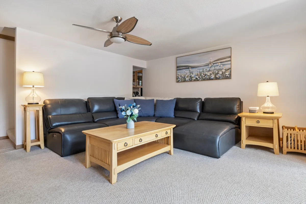 A spacious living area with a leather sectional sofa, wooden coffee table, decorative painting, and table lamps. The warm lighting and cozy furnishings create an inviting environment ideal for family relaxation and gatherings. The setting suggests a welcoming space for both people and pets to unwind together.